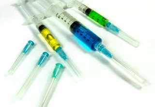 Multiple syringes with needles, filled with various colours of medicine/vaccines. three other sheathed needles of varying sizes included